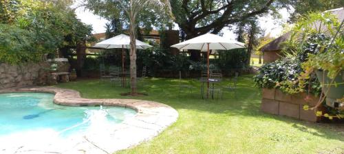 a backyard with a pool with chairs and umbrellas at Anna Boeremeisie Guesthouse in Benoni