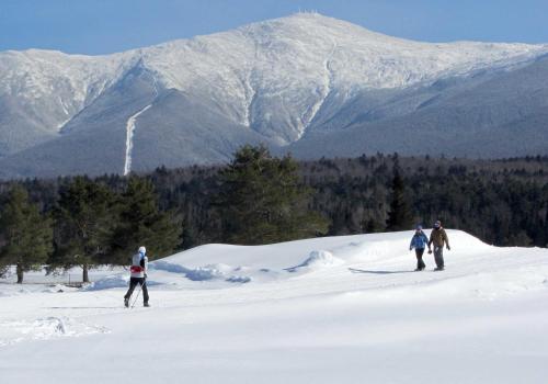 three people walking in the snow in front of a mountain at Omni Bretton Arms Inn at Mount Washington Resort in Bretton Woods
