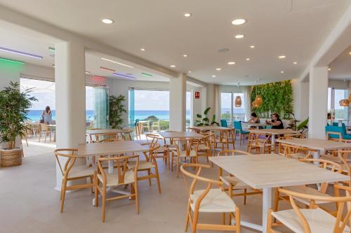 a restaurant with tables and chairs and the ocean at Hotel Maysi in Playa Migjorn