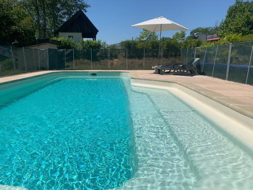 a blue swimming pool with a table and an umbrella at Chalets & Camping Villa Mayari in Escosse