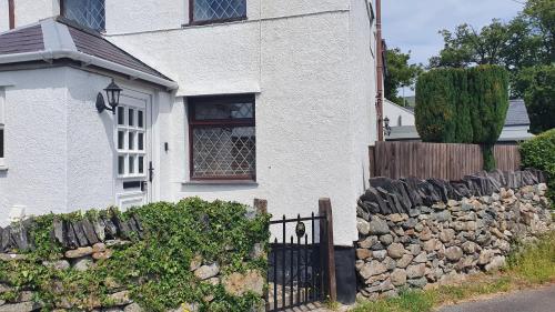 ein weißes Haus mit einem Zaun und einer Steinmauer in der Unterkunft Green Cottage - Snowdonia in Llanllechid