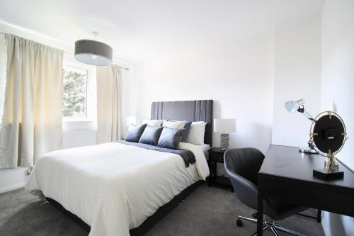 a white bedroom with a bed and a desk and a chair at Virexxa Aylesbury Centre - Deluxe Suite - 3Bed House with Free Parking in Aylesbury
