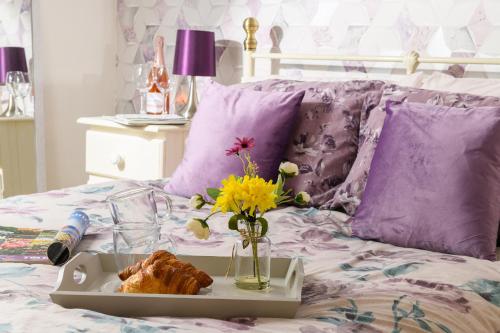 a tray of food on a bed with purple pillows at Finest Retreats - Golygfa o'r Castell - Castle Views in Harlech