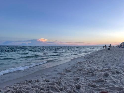 a beach with people walking on the sand and the ocean at LIVE ON ISLAND TIME! GREAT GULF SHORES BEACH CONDO, VERY NICE in Gulf Shores