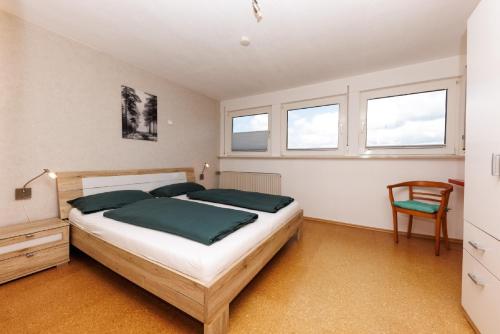 a bedroom with a bed and a chair and windows at Ferienwohnung Roth in Hilchenbach