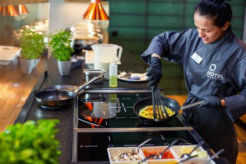 a woman cooking food in a wok in a kitchen at Q Hotel Plus Wrocław Bielany in Wrocław