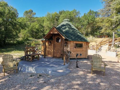 a small wooden cabin with a green roof and two chairs at La Chaumière des Elfes in Servas