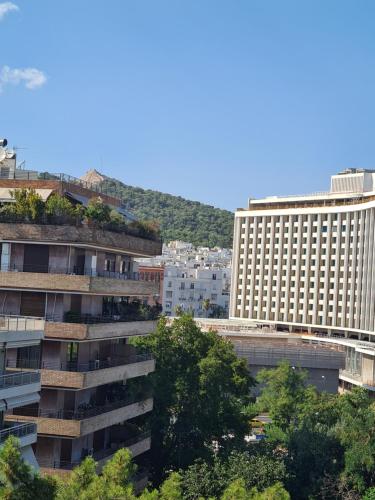 un edificio alto con árboles delante de algunos edificios en Downtown, penthouse apartment with great view, Pagkrati en Atenas
