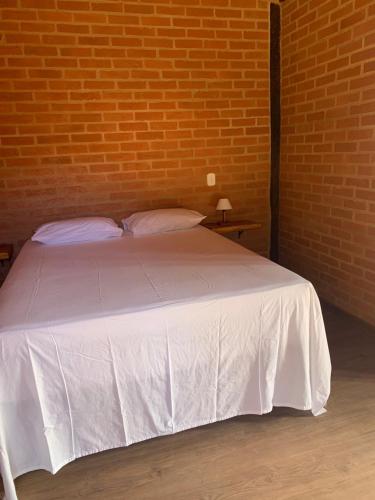 ein Schlafzimmer mit einem weißen Bett mit Ziegelwand in der Unterkunft chalés Roma in Santo Antônio do Pinhal