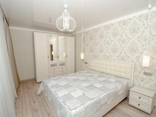 a white bedroom with a white bed and a chandelier at Jūras 4 Apartament in Ventspils