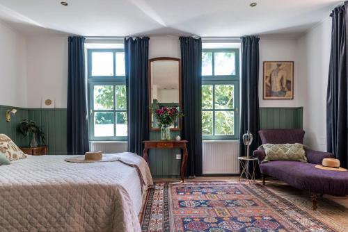 a bedroom with a bed and a chair and windows at Berky Kúria - Stylish cottage in the Hills of Tolna for 16people in Nagykónyi