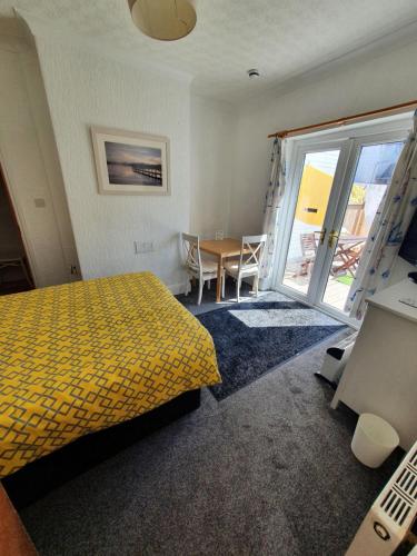 a bedroom with a yellow bed and a table and chairs at SINGER HOUSE ,PAIGNTON SEAFRONT ,SLEEPS 6 , 2 BEDROOM GROUND FLOOR SELF CONTAINED GARDEN FLAT , PRIVATE ENTRANCE , KITCHEN , Guaranteed Parking ,Wifi , Movies ,Bathroom ,fridge , microwave ,BEDROOM 1, DOUBLE BED & 2 SINGLE BEDS ,BEDROOM 2 , DOUBLE BED in Paignton