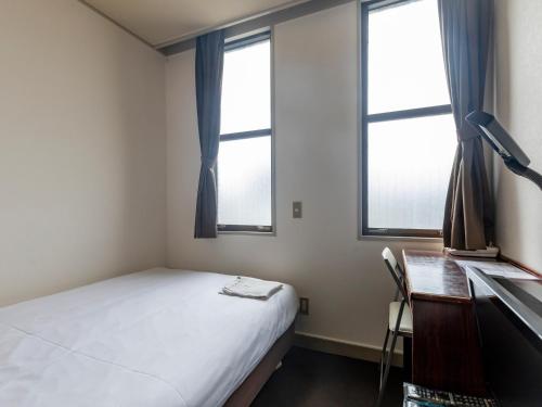 a bedroom with a bed and a desk and two windows at Tabist Business Hotel Suehiro Matsuyama in Matsuyama