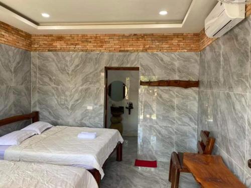 a bedroom with two beds and a stone wall at Green Bamboo Lodge Resort in Cat Tien