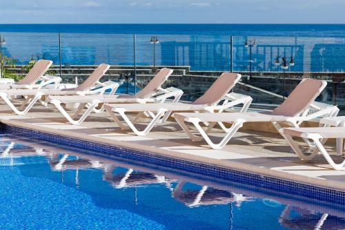 a row of lounge chairs next to a swimming pool at Hotel Monopol in Puerto de la Cruz