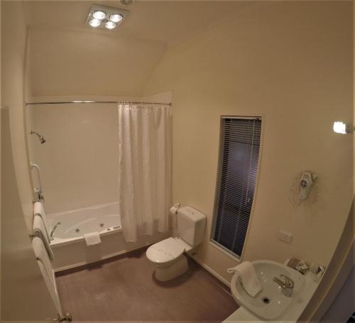 a bathroom with a toilet and a tub and a sink at The Peaks Motor Inn in Ohakune