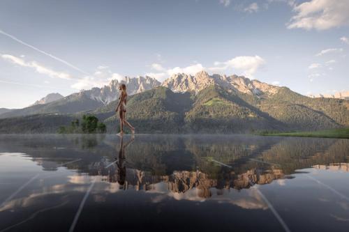 a woman standing on the water with mountains in the background at Hotel Schopfenhof in San Candido