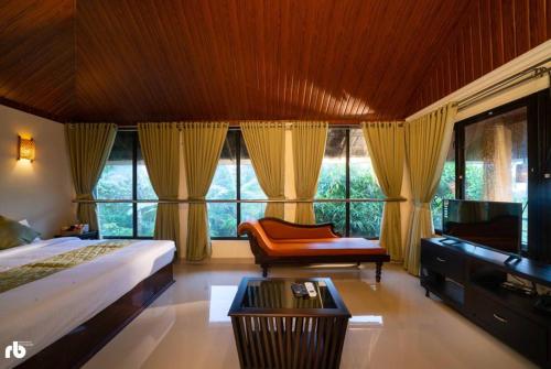 a bedroom with a bed and a chair and windows at Kuruva Isles Jungle Resort in Wayanad