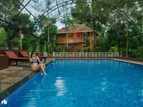 a woman sitting on the edge of a swimming pool at Kuruva Isles Jungle Resort in Wayanad