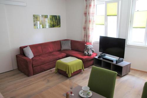 ein Wohnzimmer mit einem roten Sofa und einem TV in der Unterkunft Elli, Appartement inklusive kostenfreiem Eintritt in die Alpentherme in Bad Hofgastein