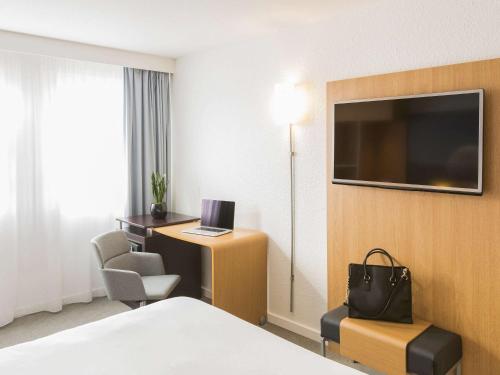 una camera d'albergo con letto, scrivania e TV di Novotel Strasbourg Centre Halles a Strasburgo