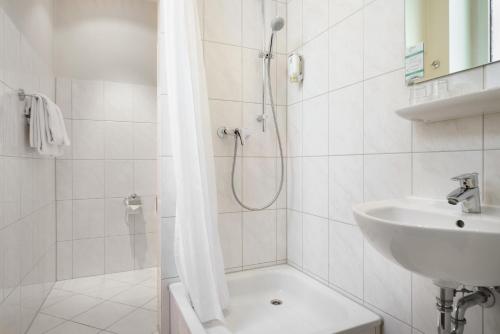 baño blanco con ducha y lavamanos en Novum Hotel Continental Hamburg Hauptbahnhof, en Hamburgo