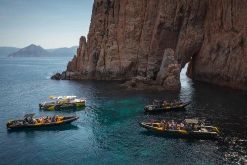 three boats in a body of water next to a mountain at Hôtel & Résidence Le Subrini in Porto Ota