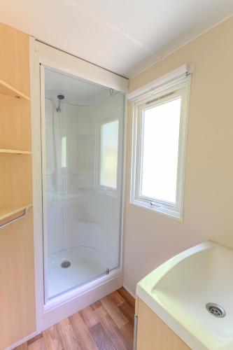La salle de bains est pourvue d'une douche et d'une fenêtre. dans l'établissement Mobil-home LE WILSON, à Mirgaudon