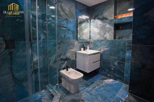 a blue tiled bathroom with a toilet and a sink at DeLux Center Apartments Inđija in Inđija