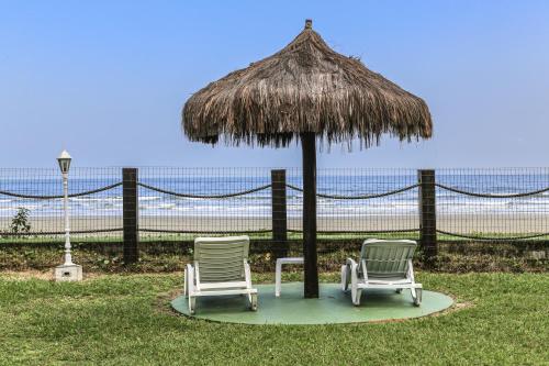two chairs under a straw umbrella on the beach at Indaiá Praia Hotel in Bertioga