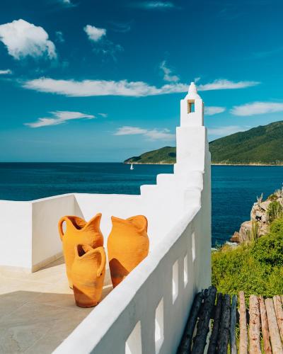 two orange vases sitting on a white wall next to the ocean at Casa Grega in Arraial do Cabo