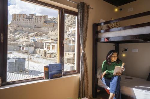 a woman sitting in a bed reading a book in front of a window at LeHostel in Leh