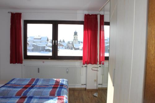 a bedroom with a window with red curtains and a bed at Seeglück in Oy-Mittelberg