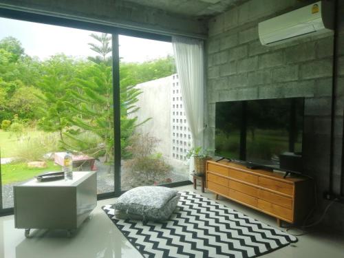 a living room with a tv and a large window at The Box Promkiri (เดอะบ๊อค พรหมคีรี) in Ban Pak Ram