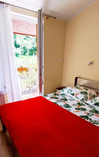 a bedroom with a bed with a red blanket and a window at Pokoje Gościnne Sonea in Lewin Kłodzki