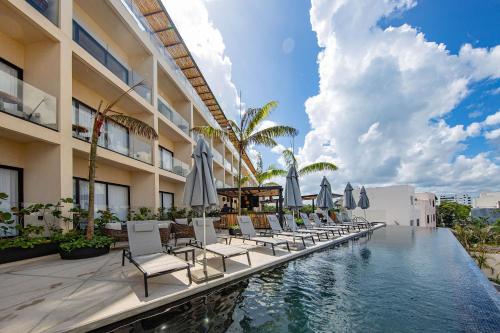 a pool with chairs and umbrellas next to a building at Hive Cancun by G Hotels in Cancún
