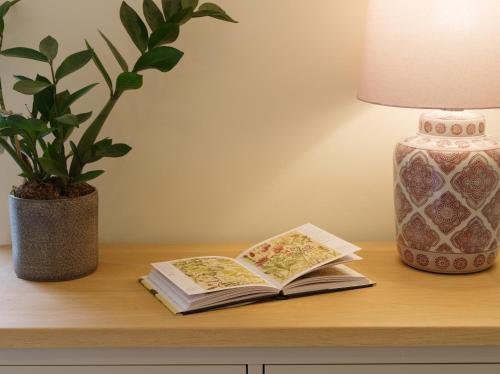 two books on a table next to a lamp and a potted plant at Garden House at Woodhall Estate in Hertford