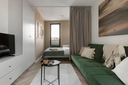 a living room with a green couch and a bedroom at Glow Apartments, Aparthotel Kołłątaja - Wrzeszcz in Gdańsk