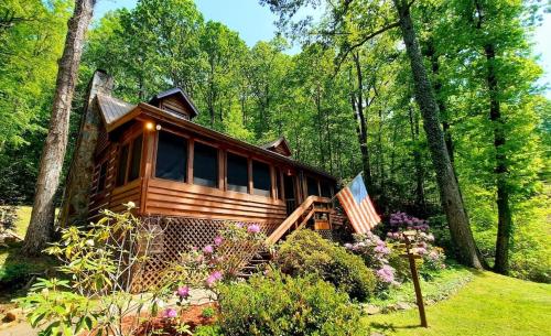 a cabin in the woods with a flag and flowers at The Mountain Forager Cabin, Whitewater Rafting, Polar Express, Hot Tub, Home Gym, SMNP, SM Railroad in Bryson City