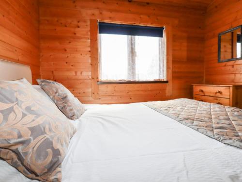 a bed in a wooden room with a window at Maple Lodge in Bodmin
