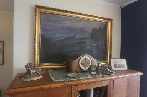 a clock on top of a wooden cabinet with a painting at Villa apartment Hafnarfjordur - Ideal for Aurora in Hafnarfjördur