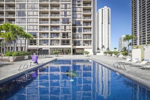 a swimming pool with chairs and a large building at Aston Waikiki Sunset in Honolulu