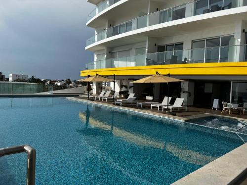 a swimming pool with chairs and umbrellas next to a building at Luxury condo en Malecón, Alberca Infinity & Jacuzzi in Mazatlán