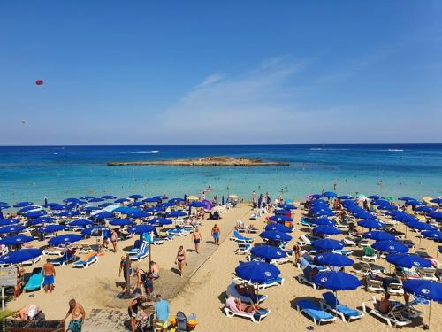 a crowd of people on a beach with blue umbrellas at Odessa Beach Hotel in Protaras