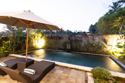 a swimming pool with an umbrella and two chairs at Villa Natha in Ubud