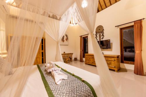 a bedroom with a bed with white curtains and a tv at Villa Natha in Ubud