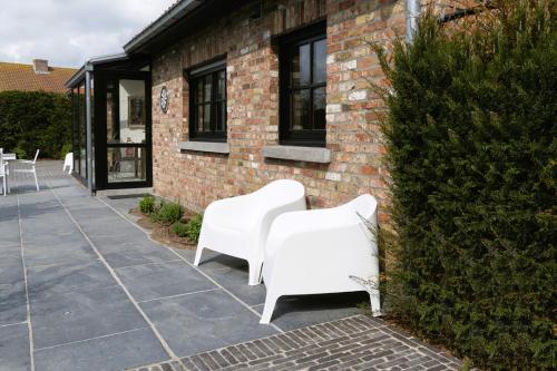 two white chairs sitting next to a brick building at Vakantievilla Leonie in Lo-Reninge