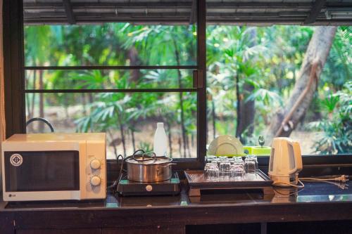a kitchen counter with a microwave and a stove with a window at Baan Suan Residence เฮือนพักบ้านสวน in Chiang Mai
