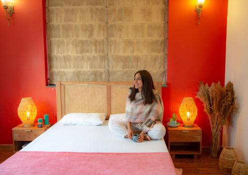 a woman sitting on a bed in a room with red walls at House of Kapaali in Greater Noida