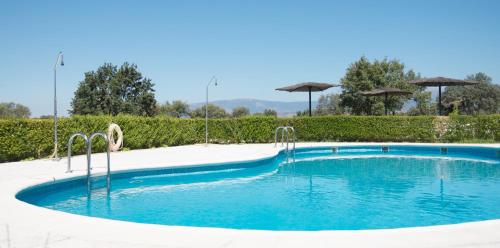 a swimming pool with blue water and umbrellas at Hospedium Hotel Valles de Gredos Golf in Talayuela